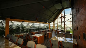 An indoor dining area with tables and chairs, large windows, and hanging pendant lights.