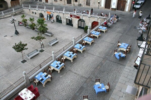 An outdoor cafe with tables and chairs, a fountain, and a building with a sign.