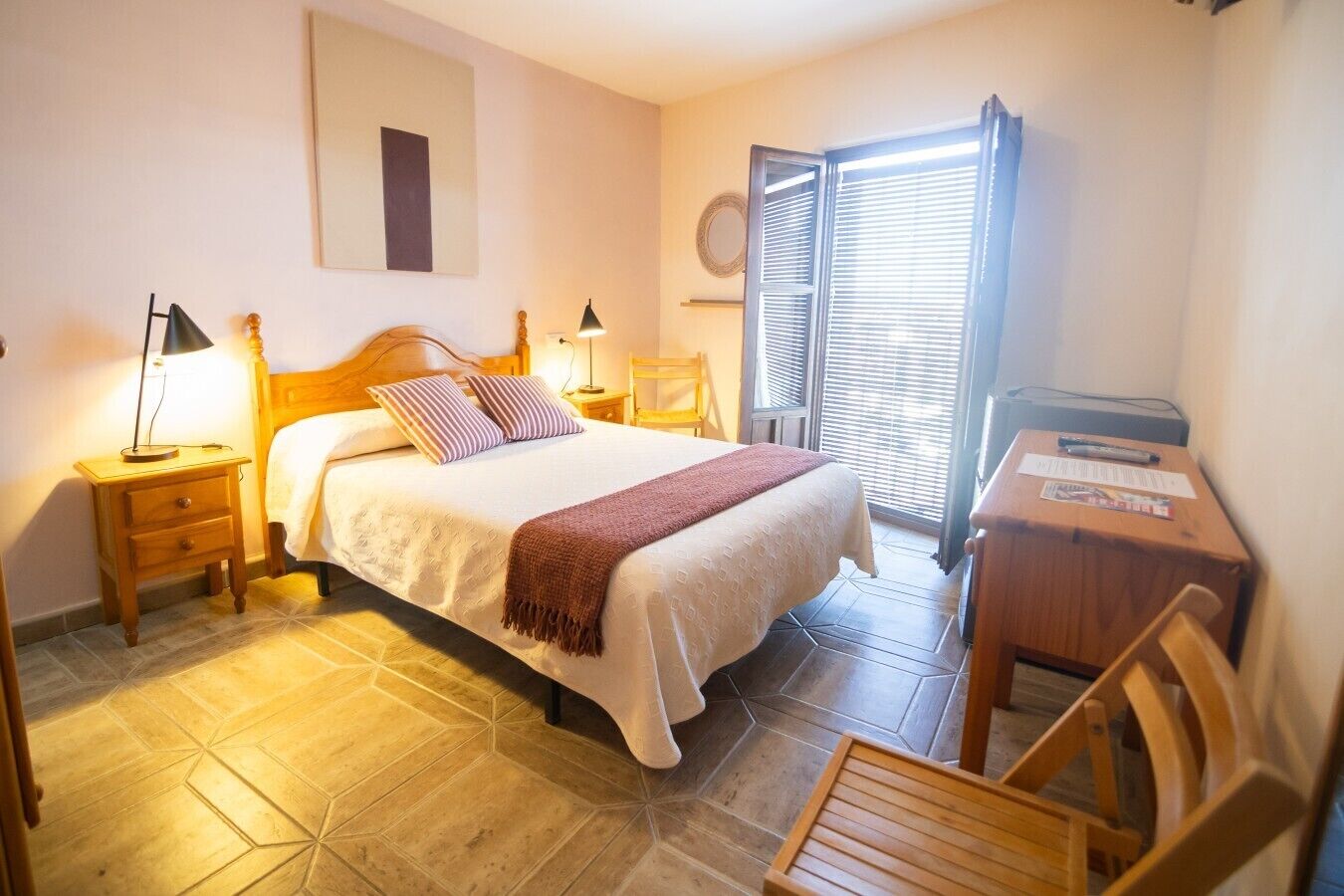 A hotel room with a bed, bedside tables, a desk, and a chair.