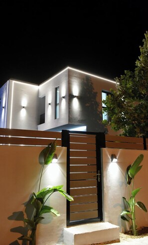 Un edificio moderno con un imponente portón negro, iluminado por luces empotradas.