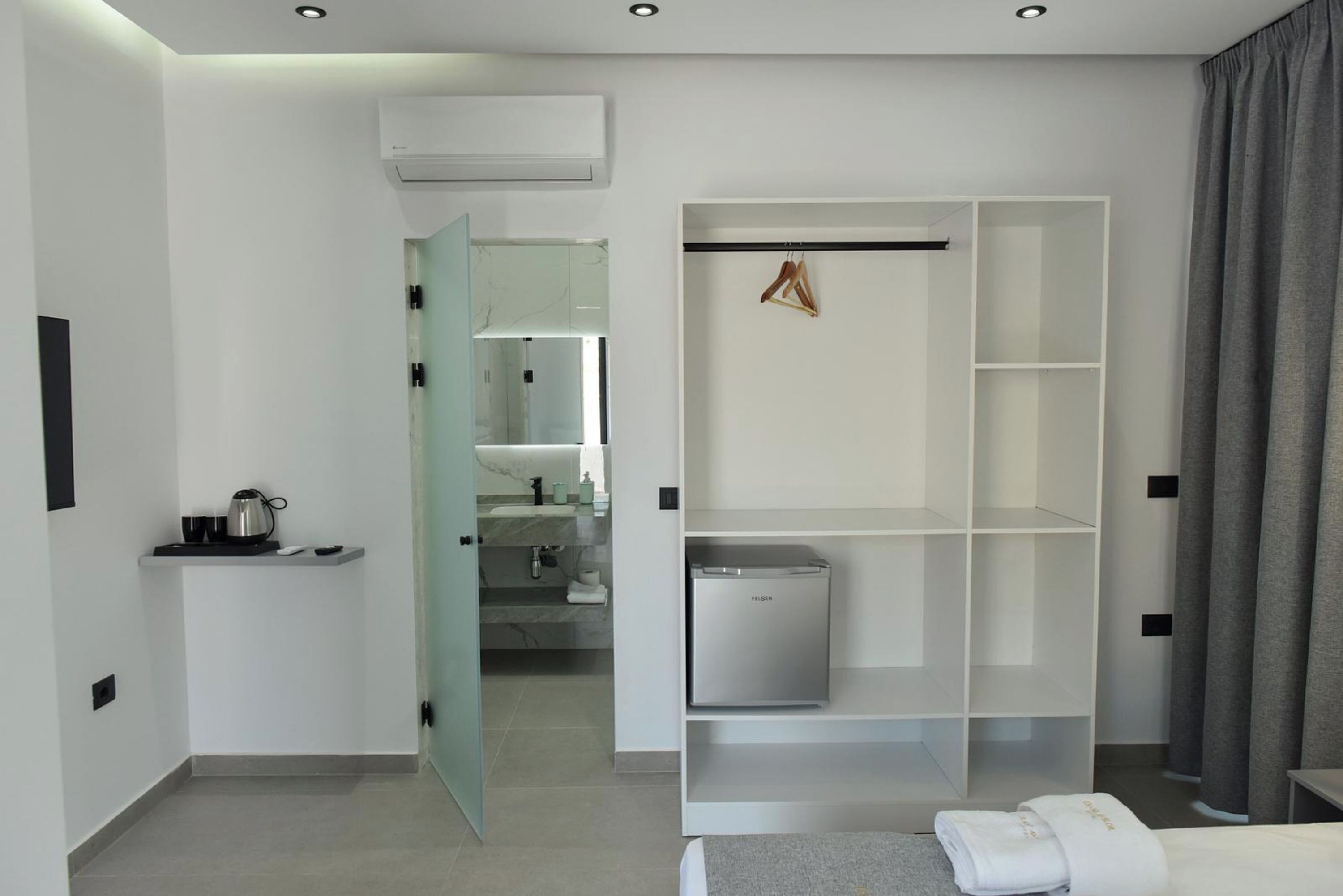 Habitación de hotel moderna con kitchenette, vestidor y baño a la vista a través de una puerta abierta.