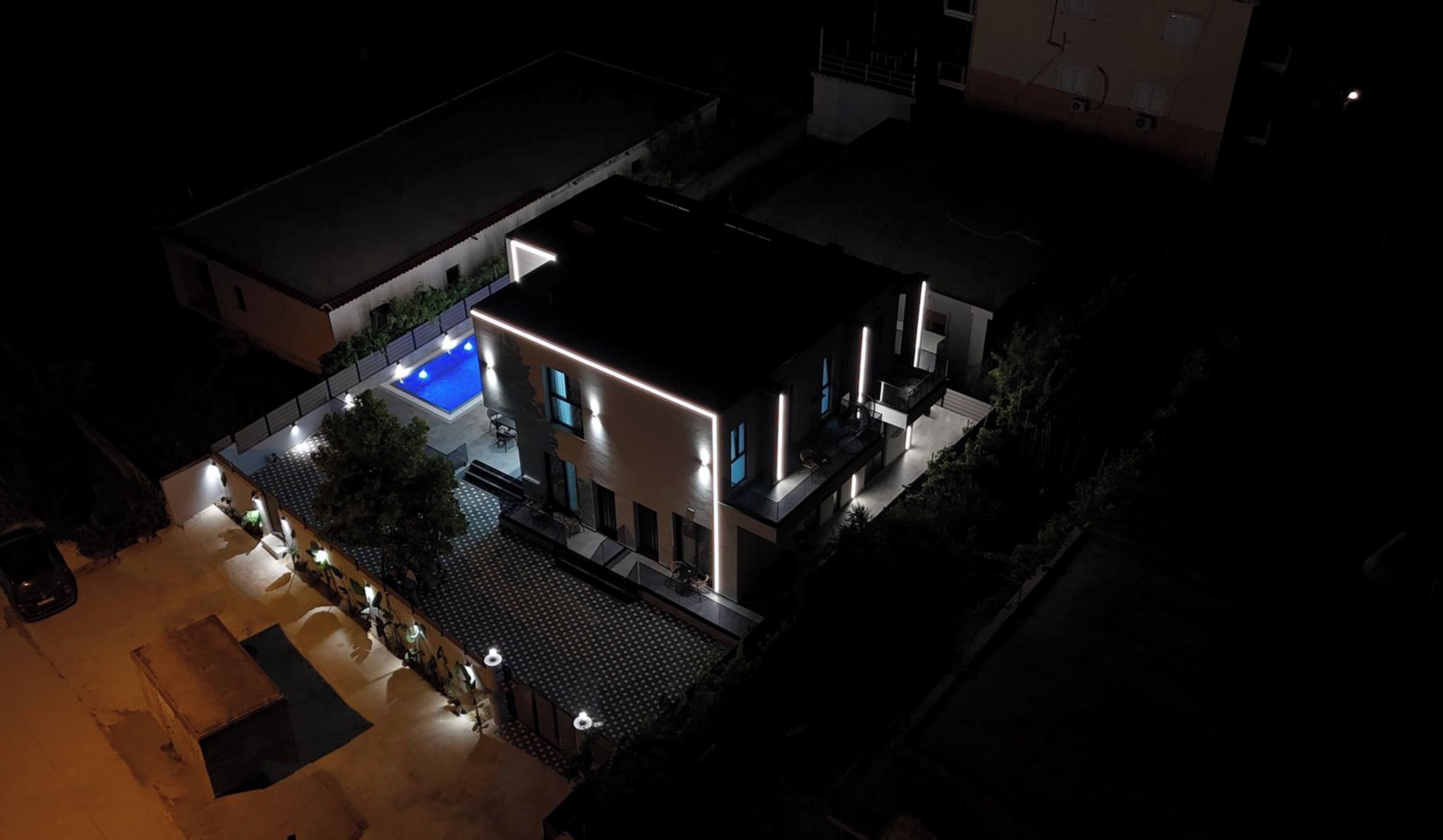 Ein modernes, zweistöckiges Haus mit Schwimmbad, Außenbeleuchtung und einer überdachten Terrasse.