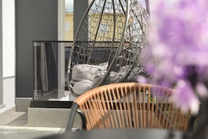 A balcony with a hanging chair, a wicker chair, and a view of a building in the background. - Grand Avelor Hotel (Vlore)