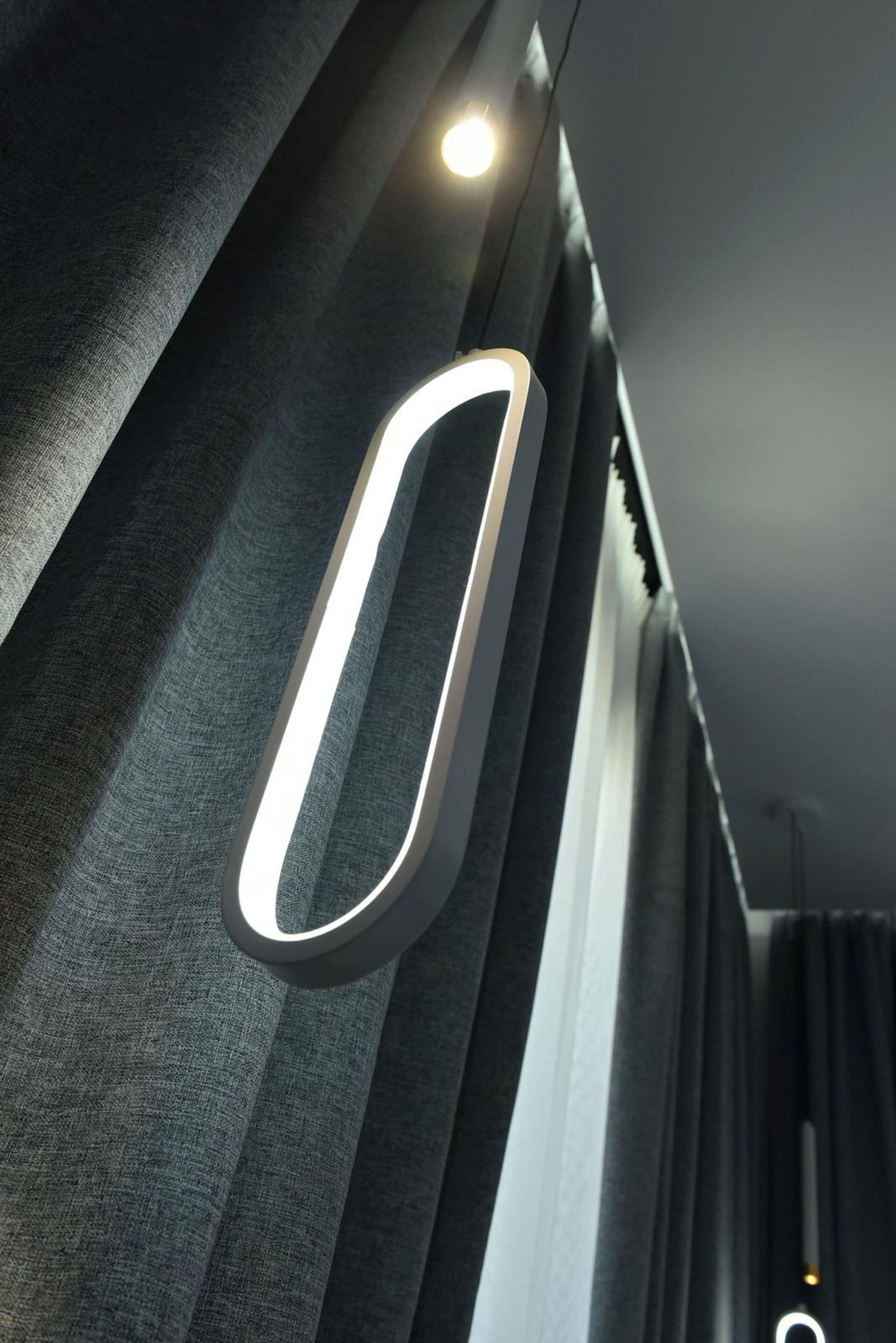 Un intérieur moderne agrémenté d’un luminaire original et de rideaux foncés.