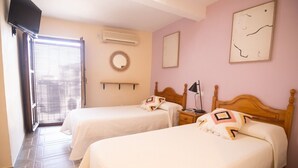 A room with two beds, a TV, an air conditioner, a mirror, and a window with blinds.