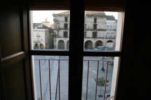Una ventana con vistas a una calle y edificios, incluyendo un arco y un coche estacionado.