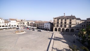 A spacious public square with a fountain, surrounded by historic buildings with arches and a prominent clock tower.