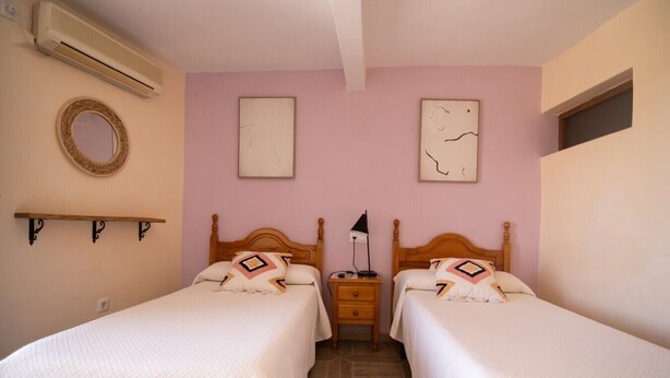 A bedroom with two beds, a bedside table, a lamp, and a wall-mounted air conditioner.