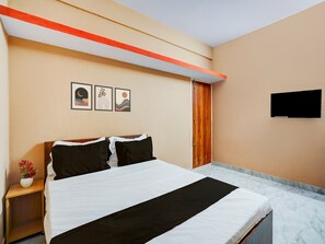 A hotel room with a bed, a nightstand with a vase of flowers, and a wall-mounted TV.