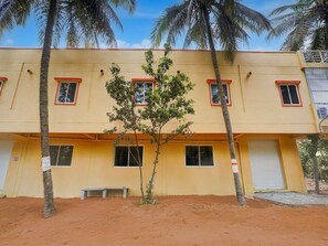 A two-story building with a yellow facade, multiple windows with red frames, and a small tree in front.