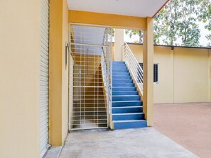 A staircase with metal railings leading to an upper floor, a closed door to the left, and a concrete ground.
