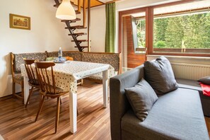 A dining area with a table and chairs, a sofa, a staircase, and a window with a view of trees. - Apartment 'Haus Behrendt' with Mountain View, Balcony and Wi-Fi (Walkenried)