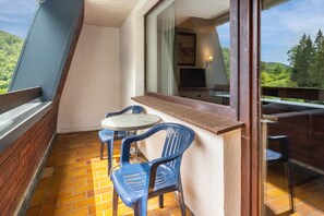 Un balcon avec une table et des chaises, une fenêtre donnant sur un paysage verdoyant et un téléviseur fixé au mur.