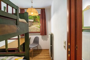 Une pièce avec un lit superposé, une chaise, une fenêtre avec des rideaux, un radiateur et une porte en bois.