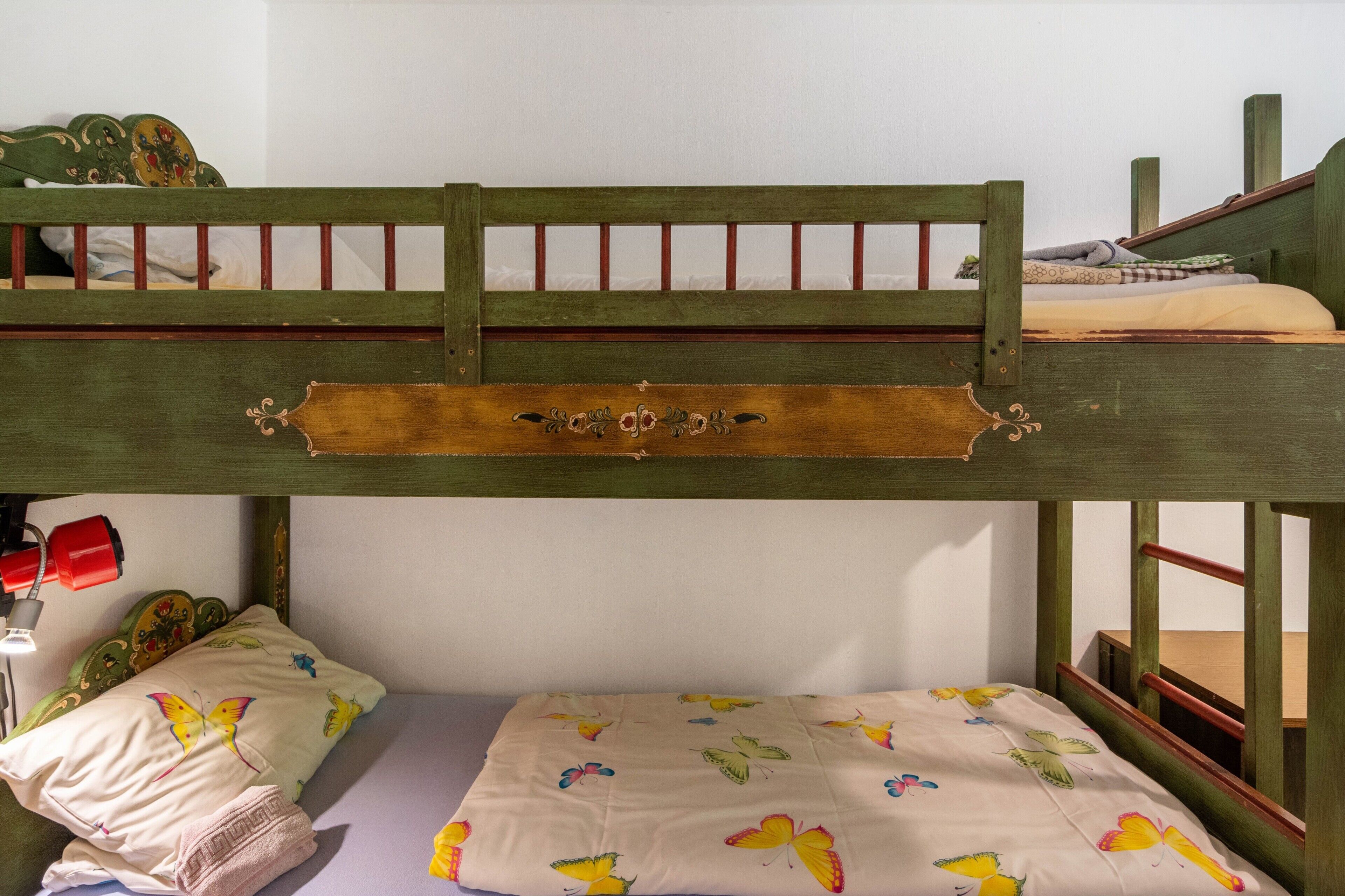 A bunk bed with a wooden headboard and a lower bed with a butterfly-patterned bedspread.