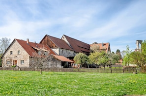 Une maison en pierre avec un toit rouge, une grange en bois et un champ clôturé.