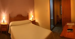 Une chambre d’hôtel comprenant un lit, des lampes de chevet, une table de chevet, une tête de lit en bois et un bureau avec une télécommande.