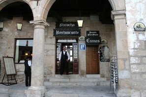 Un bâtiment avec une façade en pierre, une enseigne indiquant « Restaurant » et un panneau « P » pour indiquer un parking.