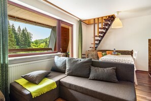 Ein modernes Wohnzimmer mit einer Couch, einem Esstisch, einer Treppe und Blick ins Freie.