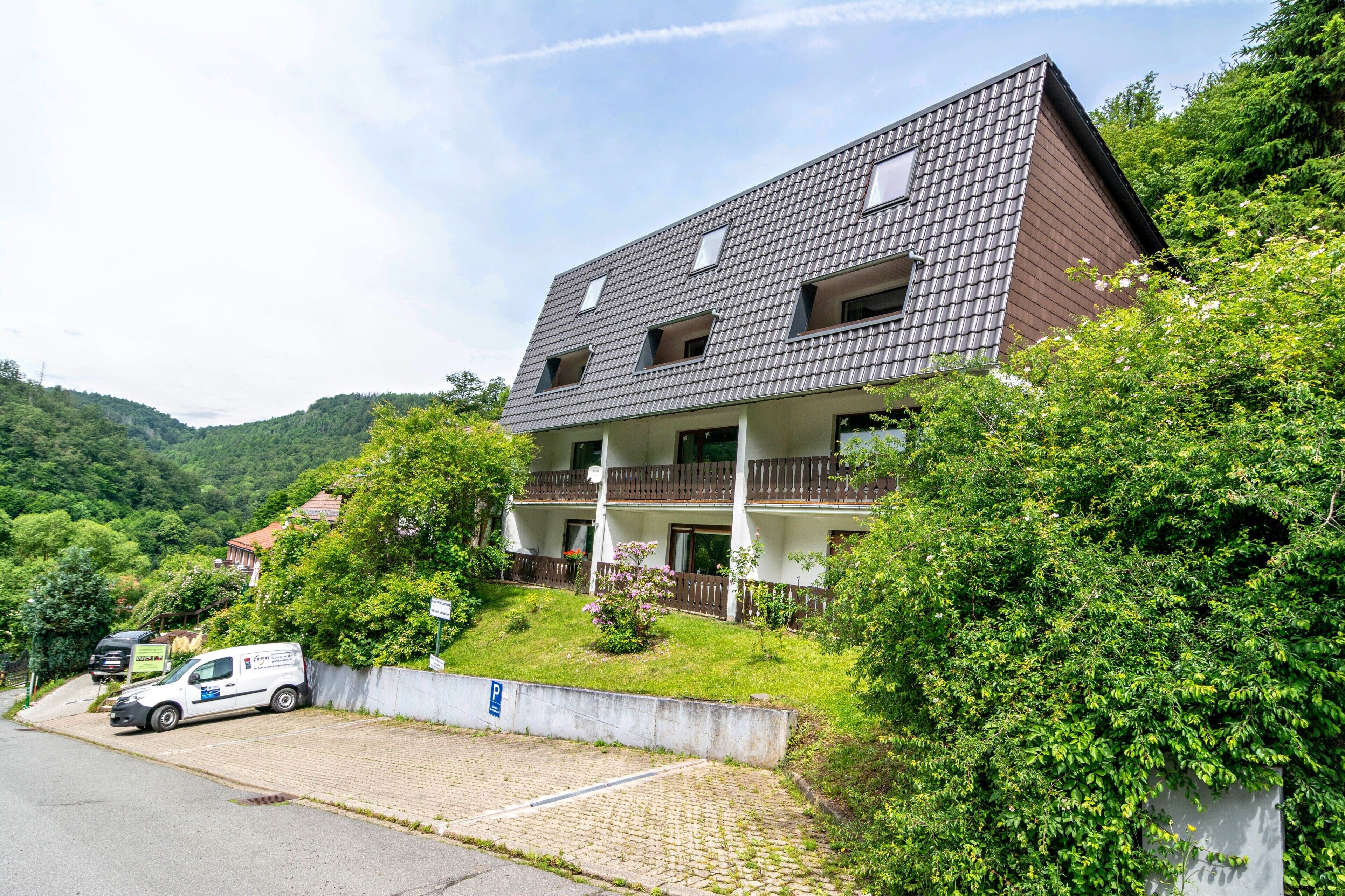A two-story building with a sloped roof, balconies, and a paved driveway.