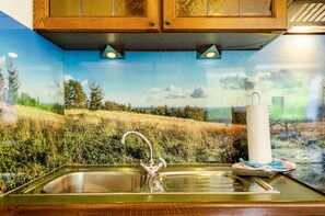 Eine Küche mit Spüle aus Edelstahl, Holzschränken und einem Wandbild einer Landschaft.