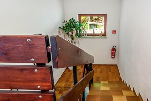 Eine Treppe mit hölzernen Bänken, einem Feuerlöscher und einem Fenster mit Blick auf Grünflächen.