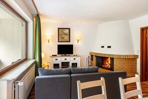 Ein Wohnzimmer mit Kamin, einer Couch, einem Fernseher und einem Fenster mit Vorhängen.