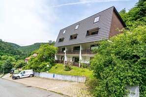 Ein zweistöckiges Gebäude mit geneigtem Dach und einem Balkon im zweiten Stock sowie einem gepflasterten Auffahrt.