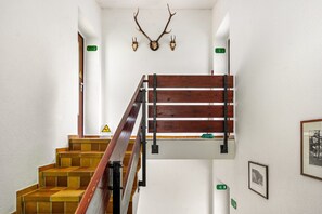 A staircase with a wooden handrail and a metal support structure, flanked by white walls with mounted deer antlers and framed pictures. - Apartment 'Haus Behrendt' with Mountain View, Balcony, and Wi-Fi (Walkenried)