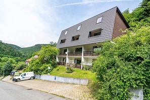 A two-story building with a sloped roof, a balcony on the second floor, and a paved driveway. - Apartment 'Haus Behrendt' with Mountain View, Balcony and Wi-Fi (Walkenried)