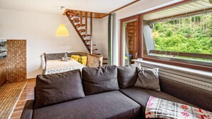 Ein modernes Interieur mit einer Couch, einem Esstisch mit Stühlen, einer Treppe und einem Fenster mit Blick auf Grünflächen.