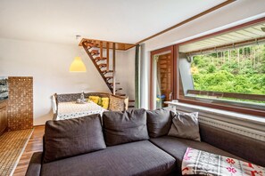 Ein modernes Interieur mit einer Couch, einem Esstisch mit Stühlen, einer Treppe und einem Fenster mit Blick auf Grünflächen.