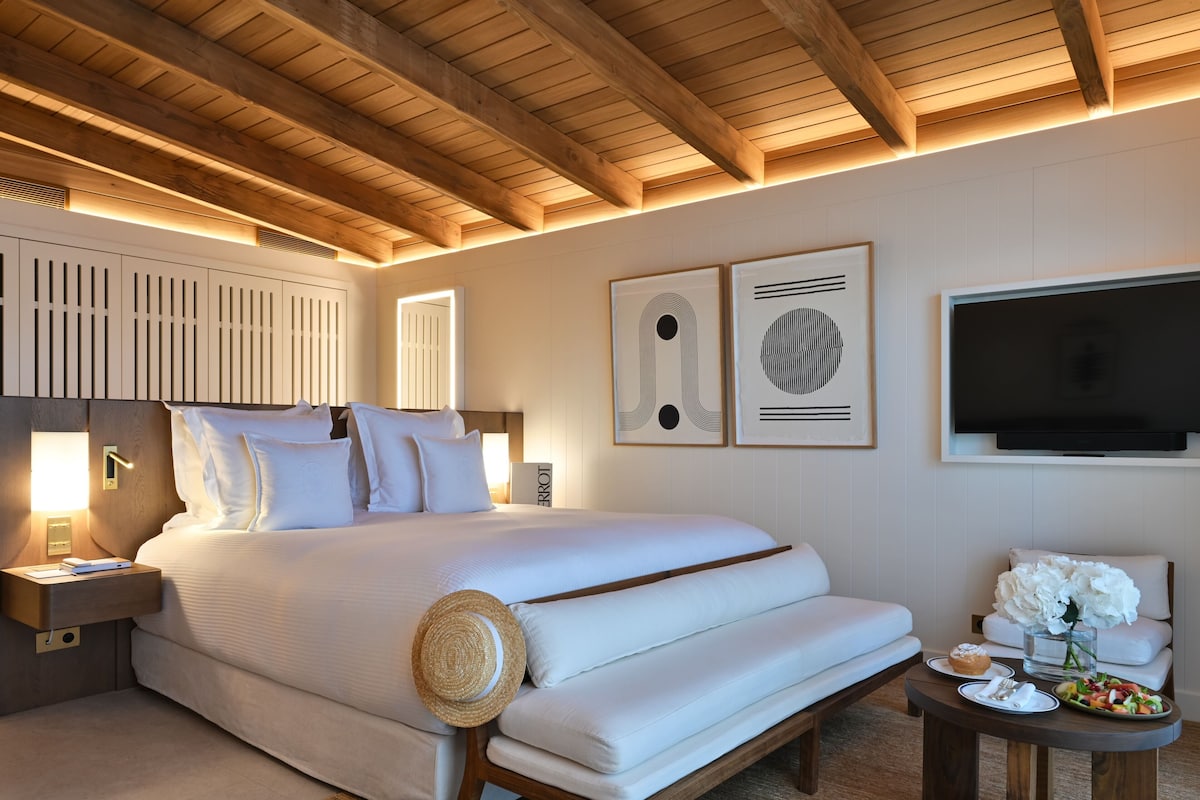 A modern hotel room with a large bed, a flat-screen TV, a bedside table with a lamp, and artwork on the walls.