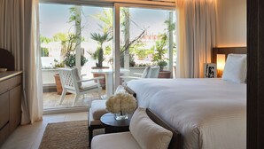 A hotel room with a large bed, a desk with a chair, a small table with flowers, and a view of the outdoor patio.