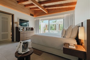 A bedroom with a bed, a TV, a desk, and a window with curtains.