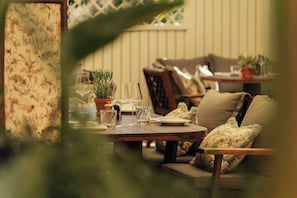A cozy dining area with a table set for two, surrounded by comfortable seating and potted plants.