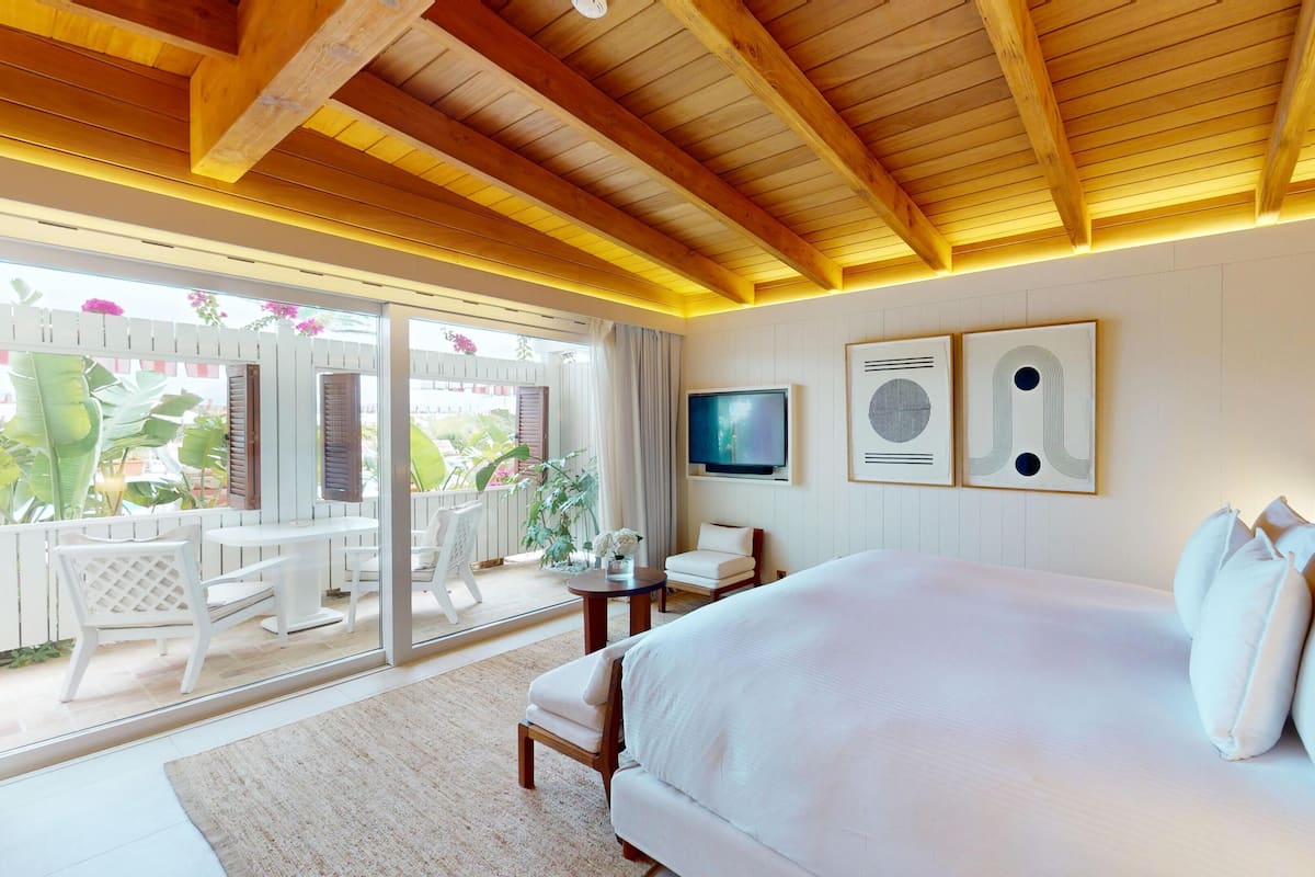 A hotel room with a large bed, a TV, and a balcony with a view of greenery.