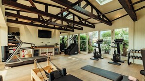 A gym with exercise equipment, wooden beams, large windows, and a television.