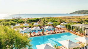 A pool area with lounge chairs and umbrellas, a clear view of the sea, and a distant lighthouse.