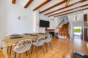A spacious dining area with a long table, white chairs, and a fireplace.