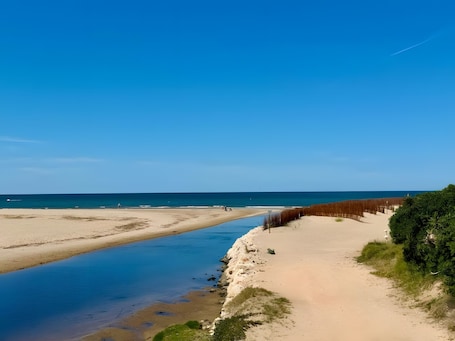 A beach with a clear sky, a sandy shore, and a calm sea.. Casa adosada villa rivera – Beachfront townhouse in Les Deveses, Dénia