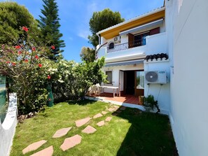 Uma casa de dois andares com varanda, um pequeno jardim com pedras para pisar, e fachada branca.