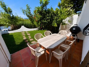 Um pátio externo com mesa e cadeiras, churrasqueira e vista para o jardim.