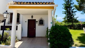 Um edifício de dois andares com telhado de telhas, entrada central com porta e uma pequena varanda com grade.