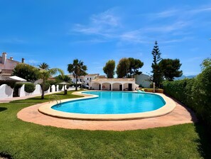 A swimming pool with a curved edge, surrounded by a paved walkway and lush greenery.