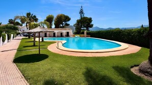 Piscina com deck ao redor, estrutura com telhado de palha e vista para montanhas distantes.
