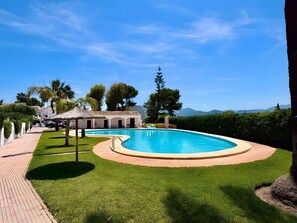 Piscina com deck ao redor, estrutura com telhado de palha e vista para montanhas distantes.