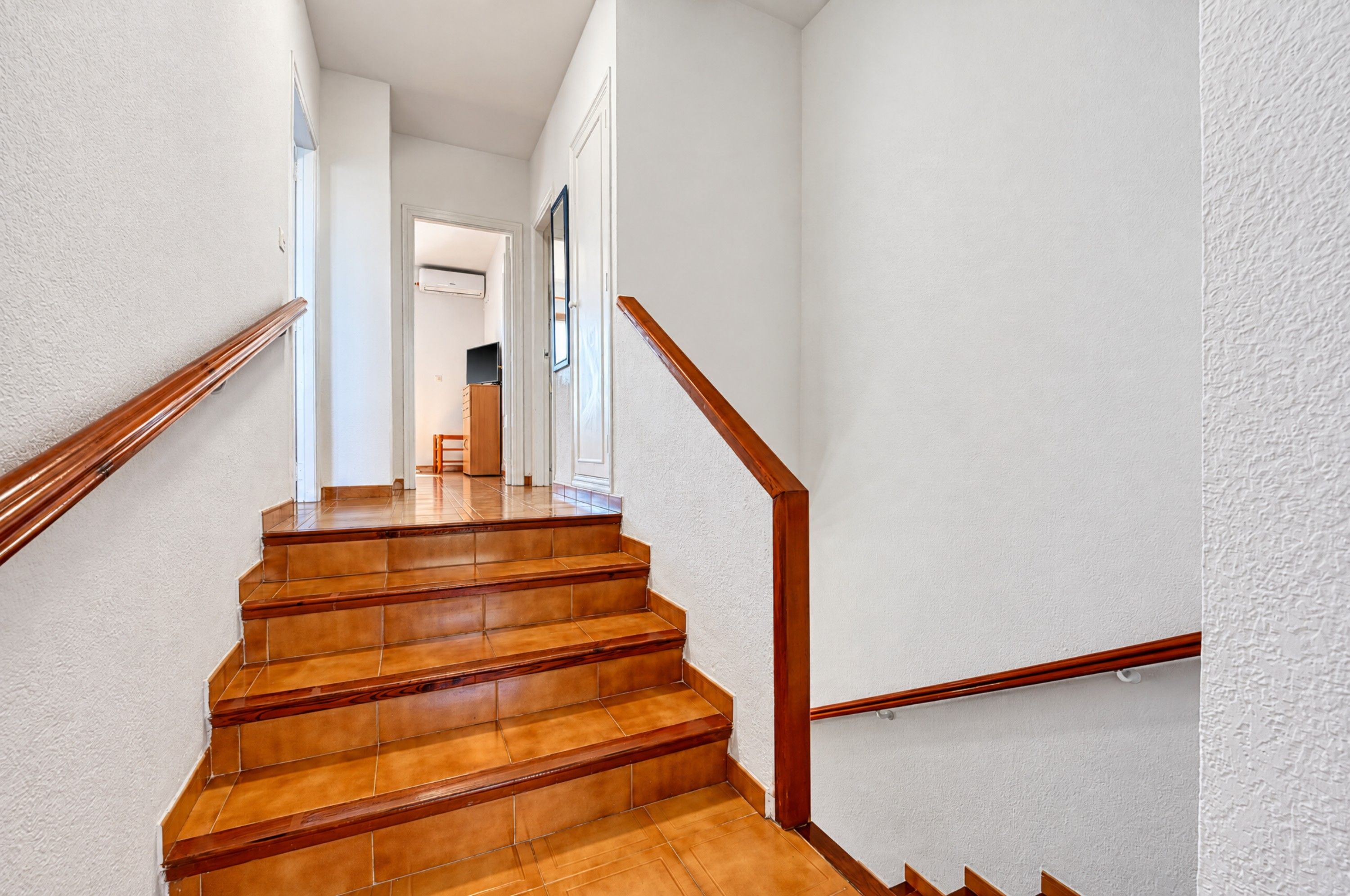 A staircase with wooden steps and a handrail, leading to a room with a door and a window.