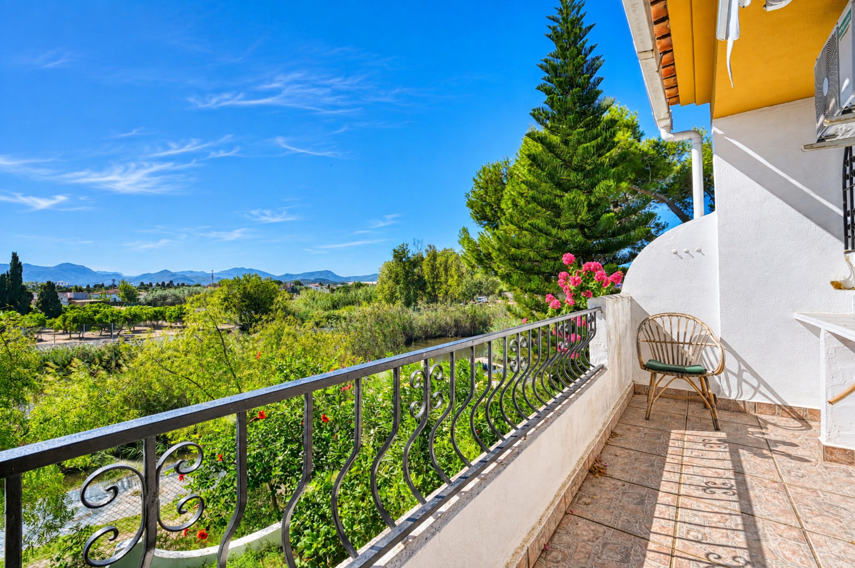 A balcony with a view of a garden and distant mountains.