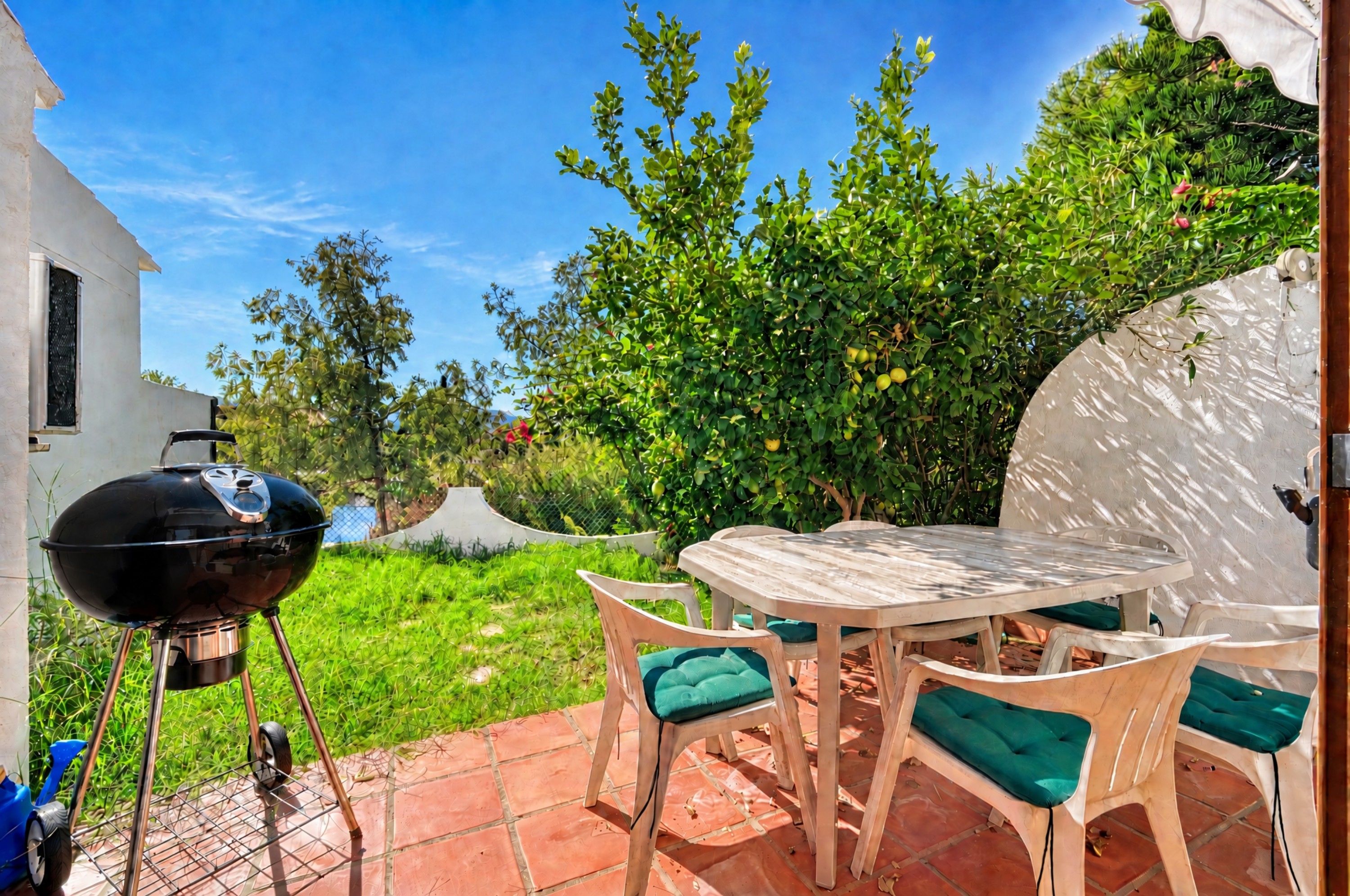 An outdoor patio with a round table and chairs, a barbecue grill, and a white building in the background.